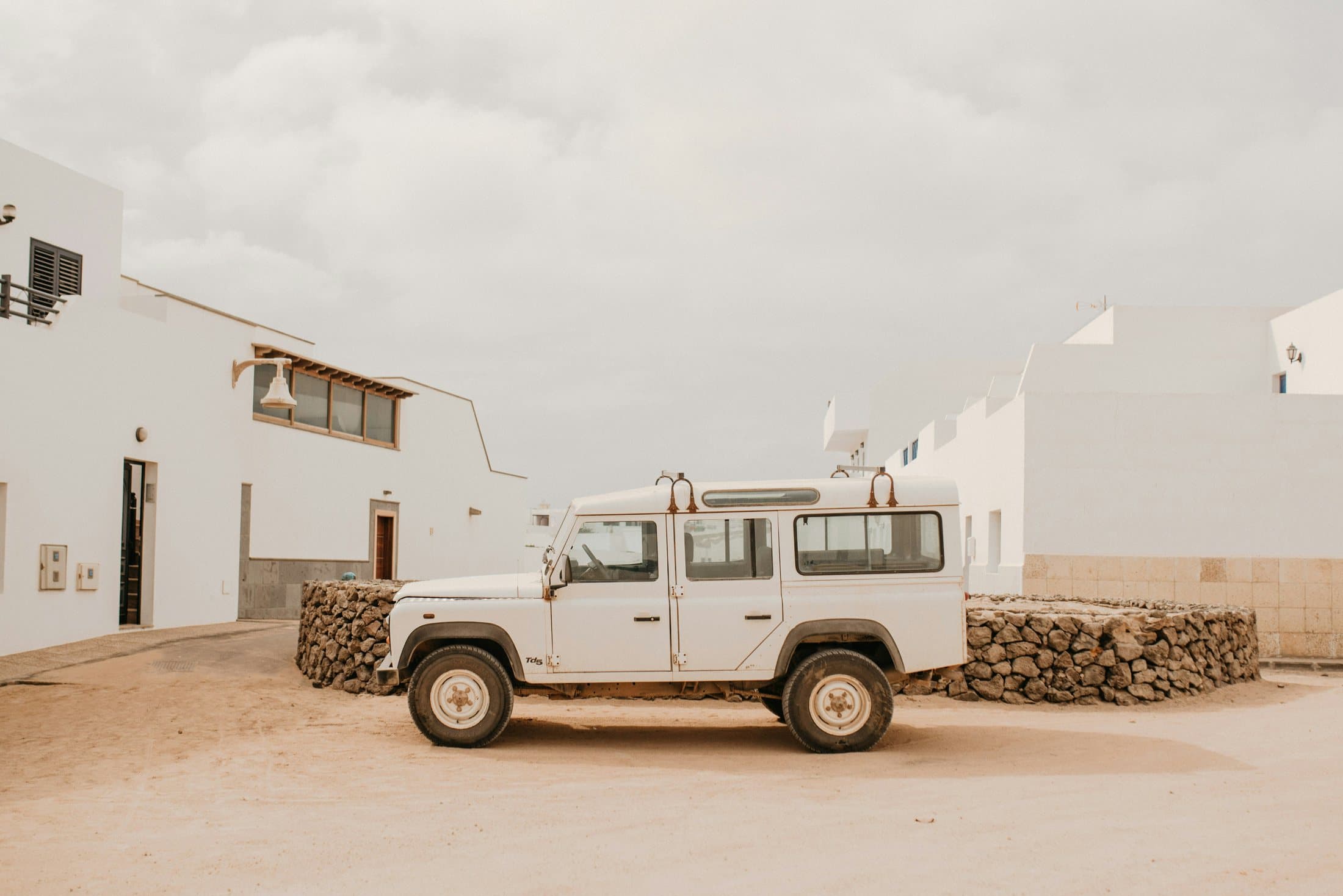 A vehicle parked beside whitewashed buildings under a pale sky